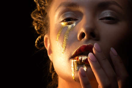 Gold on the skin, face art and creative makeup, gold as tears and blood on the face of a mysterious woman, mystical priestess, conceptの写真素材