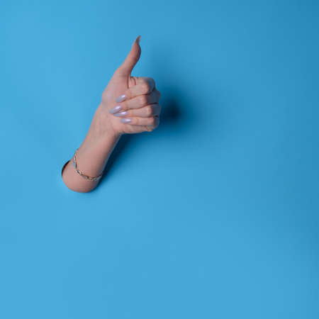 Super class, thumbs up gesture, like the concept. Hand gesture in a cardboard hole, blue backgroundの写真素材