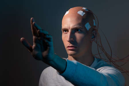 A young man with his head entangled with wires, electrical contacts on his bald head, signals to the brain. Neurointerface, future technologies, creative concept.の写真素材
