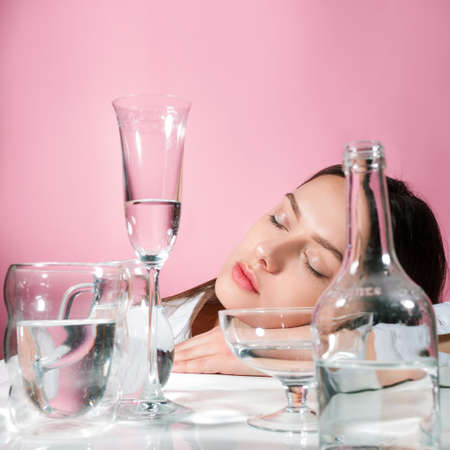 A beautiful young brunette among glasses of clean water, the benefits of clean water for beauty and health, concept. Parts of the face are refracted in a glass of waterの写真素材