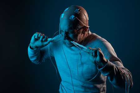 A young man with his head entangled in wires is trying to pull out electrical contacts from his head, signals to the brain. Neurointerface, future technologies, creative concept.の写真素材