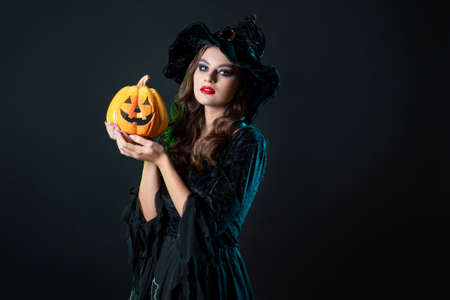beautiful witch in a pointed hat Holding a pumpkin with a laughing face, Jack lantern. Halloween party, witches  Sabbath. Young beautiful brunette in witch costume,の写真素材