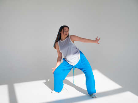 Youth jazz-funk dance style. Young and free, dancing in baggy clothes in a bright white hall. Stylish brunette in blue pants in a dynamic poseの写真素材