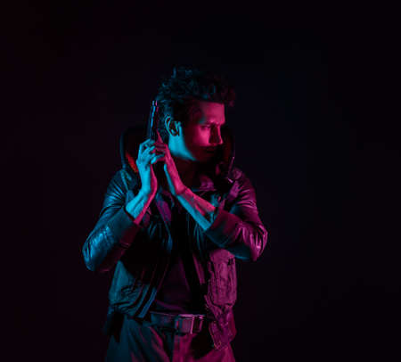 A guy in a cyberpunk image, holding a gun in his hands. Futuristic character. A young man in neon lighting on a black backgroundの写真素材