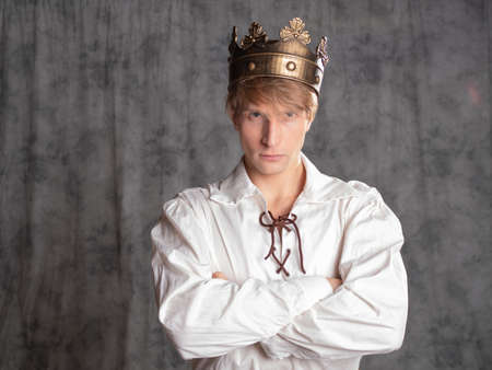 young king, man from people usurped throne, a charismatic man in a simple white blouse with lacing and with a crown on his head, a character of historical fantasy, a photo in the studio on a grayの写真素材