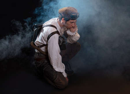 A guy in a steampunk image, a pilot or a mechanic. Retro style, fantastic image. portrait in smoke. Sitting on the floorの写真素材