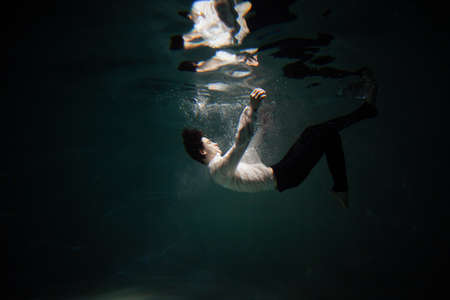Sink. A young man is going to the bottom. A guy in a white shirt and trousers falls under the water, calmness and acceptance of fateの写真素材
