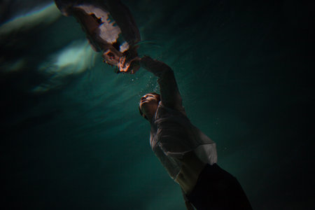 Photo underwater, a guy in a white shirt floundering underwater and reaching for the surface of the water, a man and his reflection. mystical underwater portraitの写真素材