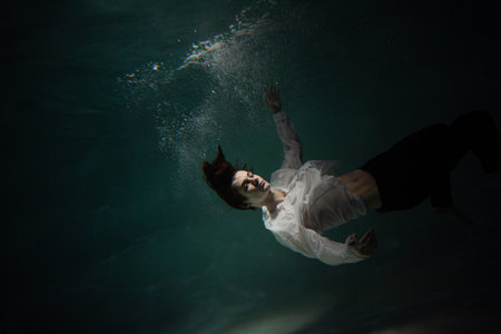 Sink. A young man is going to the bottom. A guy in a white shirt and trousers falls under the water,...