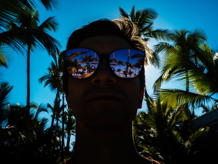man in sunglasses looks at palm trees, the reflection of palm trees in mirrored glasses. Enjoy a vacation at the seaの写真素材