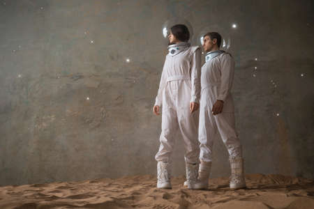 a man and a woman in white futuristic spacesuits explore the planet, astronauts in an empty colony on the sand, a holographic star map on the backgroundの写真素材