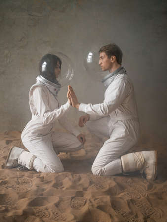 Astronauts on a deserted planet, a man and a woman in white spacesuits with large glass helmets sit...
