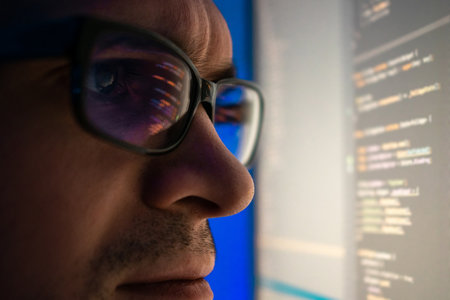 A programmer, a man in front of a computer, the code is reflected in the glasses. Working in IT,...