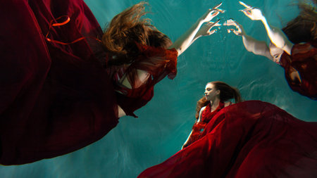 Photo underwater collage, a young beautiful woman in red with red hair reaches for the surface of the water, a human and his reflection. mystical underwater portraitの写真素材