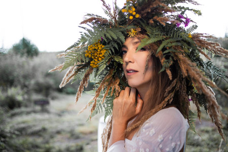 A young happy woman in a large wreath of ears and field grasses, folk-style costume, close-upの写真素材