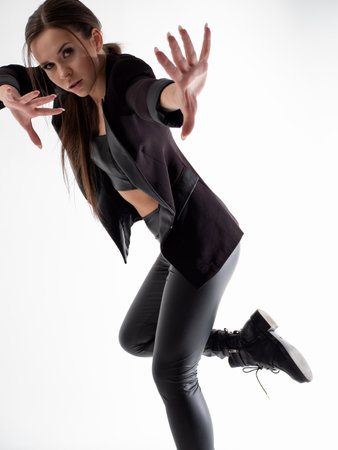 Stylish young woman in a black hat and jacket, dancing in the studio on a white background