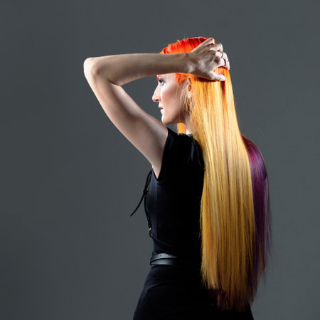 Creative hair coloring. A young woman with bright red hair with yellow and purple strands, back viewの写真素材