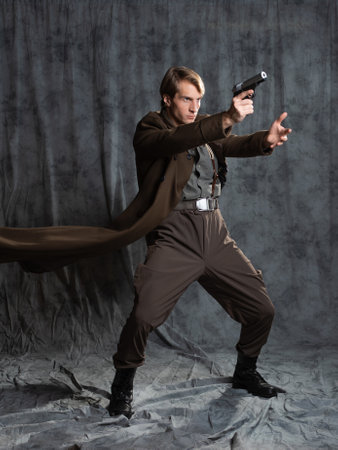hero in a military style with a gun in his hands, a young man in a long brown coat and breeches with suspenders. he shoots a pistol in a spectacular pose, his coat flutters behind his backの写真素材