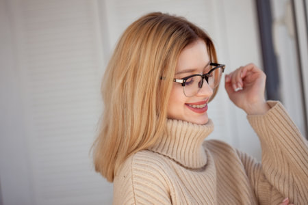 Young cute blonde with eyeglasses and a beige sweater. Stylish fashionable young woman. woman with glasses smilingの写真素材