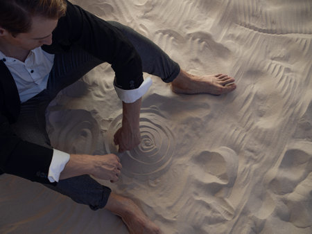 sad financier is frustrated, a young man with big plans is faced with a global economic crisis, concept. businessman in a suit is sitting on a pile of sandの写真素材