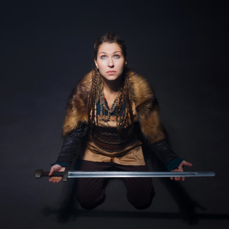 A young brave Viking heroine gazing up sitting on the floor. A young woman in a suit in Scandinavian or fantasy styleの写真素材