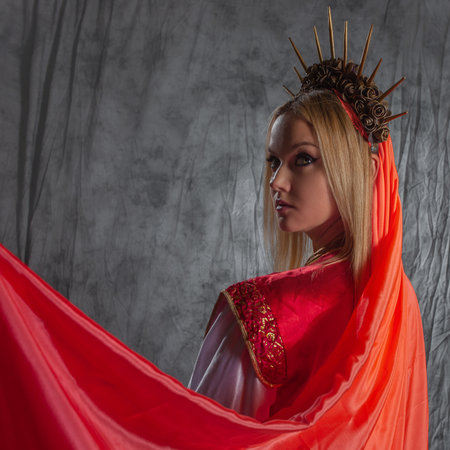 A beautiful young woman in a fantasy costume with a red veil and a golden crownの写真素材