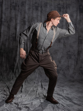 A young man in retro style, an adventure character. A guy in a hat and a gray shirt, breeches with suspenders.の写真素材