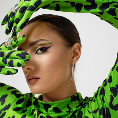 Extravagant eye makeup with bright green arrows, stylish young woman in a green leopard bodysuit, studio portrait close-upの写真素材