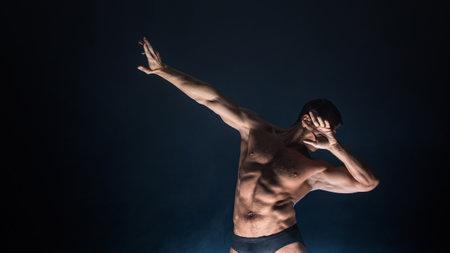 Muscular athlete in an epic pose, dark background, bright light from below, the concept of sports and bodybuildingの写真素材