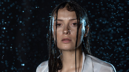 young woman in the rain, getting wet through, wet clothes and water running down her face.