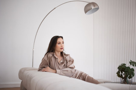 Stylish and confident brunette sitting on the couch, comfortable lifestyle. A woman in a comfortable beige oversize suit.の写真素材