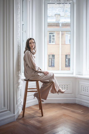 Stylish and elegant brunette sitting by the window on a high chair, portrait in the interior,sunlightの写真素材