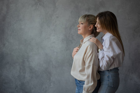 Happy family, women together. Mom and adult daughter smile at each other, studio photo in casual...
