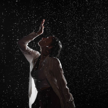 Dancing in the rain. A young woman in wet clothes dancing among water droplets, photo in the aqua studio. beautiful silhouette, model in a white shirtの写真素材
