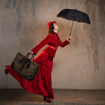 A stylish lady in a red old-fashioned suit with a hat and a lace umbrellaの写真素材