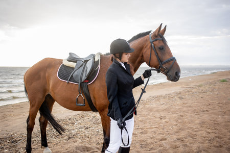 Equestrian sports. Horsewoman and her horse on the beach, portrait on the background of the sea, horseback riding outdoorsの写真素材
