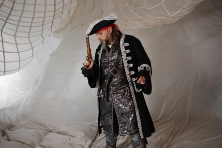 A brave captain with a doublet and a cocked hat, a sailor and a pirate, a portrait of a man in a carnival costume, sails on the backgroundの写真素材