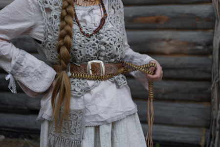 a young girl with a long blond braid in a folk costume, in a village among wooden architecture,...