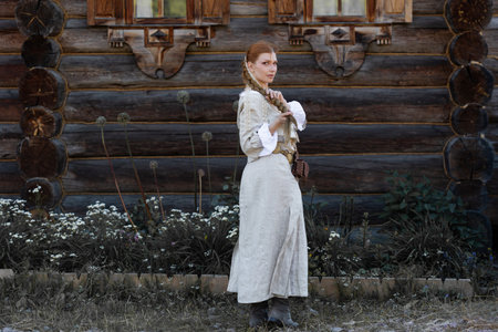a young girl with a long blond braid in a folk costume, in a village among wooden architecture,...