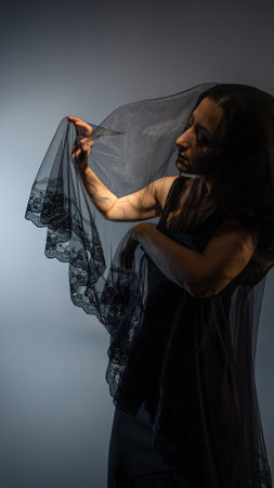 beautiful image in the Gothic style shows a young woman with black hair, wearing a black dress and a veil that hides her face. The folds of the veil drape around her figure in a mysterious way, creating a sense of mystery.の写真素材