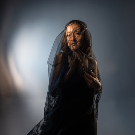 A Gothic bride, a mysterious Halloween image, a Gothic gloomy aesthetic. An elegant young woman in a black dress and with a veil on her faceの写真素材