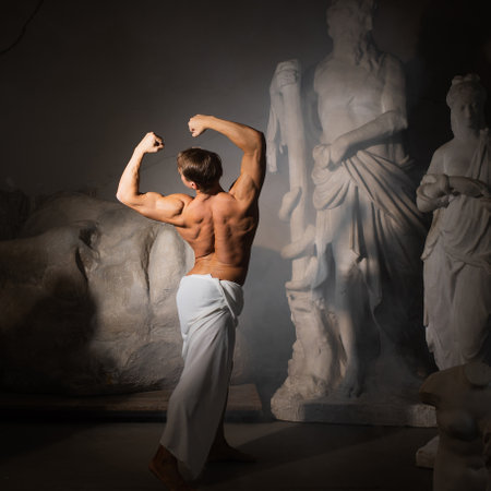 A sculptors workshop, a muscular man in a tunic among antique statues. Bodybuilder and model, aesthetics of harmonious development of the bodyの写真素材