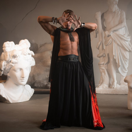 A muscular charismatic bodybuilder in a silk cape among sculpturesの写真素材