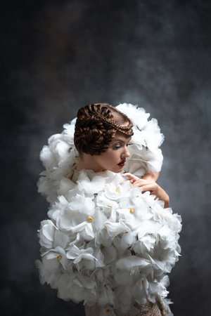Gorgeous young woman in an extravagant dress with sleeves made of flowers, studio fashion photoの写真素材
