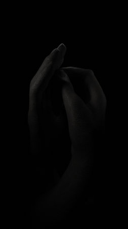 Hands clasped in a protective pose, a dark sculpture on a dark backgroundの写真素材