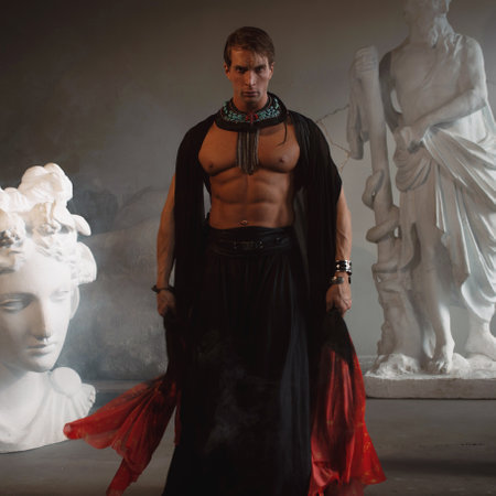 Muscular charismatic bodybuilder model in a silk cape makes an expressive pose, sculptors workshopの写真素材