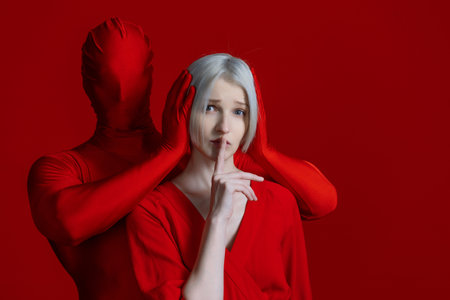 To restrain yourself, a concept. Something within me and something outside of me, makes me feel silent, externally and internally condemned. Mysterious red hands gag a woman in a red dress against a red backdrop.の写真素材