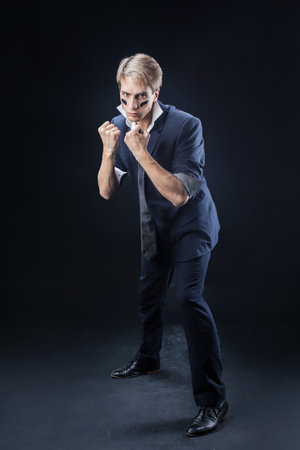 In a dimly lit studio, a man in a navy suit adopts a boxing stance, showcasing strength and determination. The sleeves are casually rolled up, enhancing his confident, dynamic pose.の写真素材
