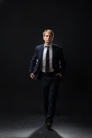 confident man strides forward in a dark suit, exuding authority and professionalism. The low-key, dark background highlights the formal attire in a corporate settingの写真素材