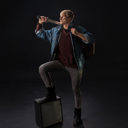 young student in a denim jacket and maroon sweater stands confidently in a studio, holding books and a sword.の写真素材